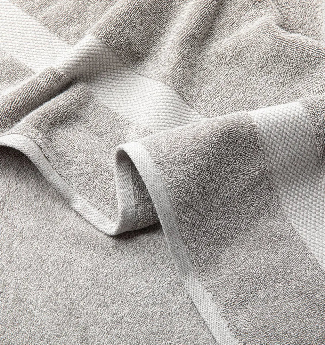 Close-up of a textured Premium Turkish Cotton gray towel with folds on a light gray background