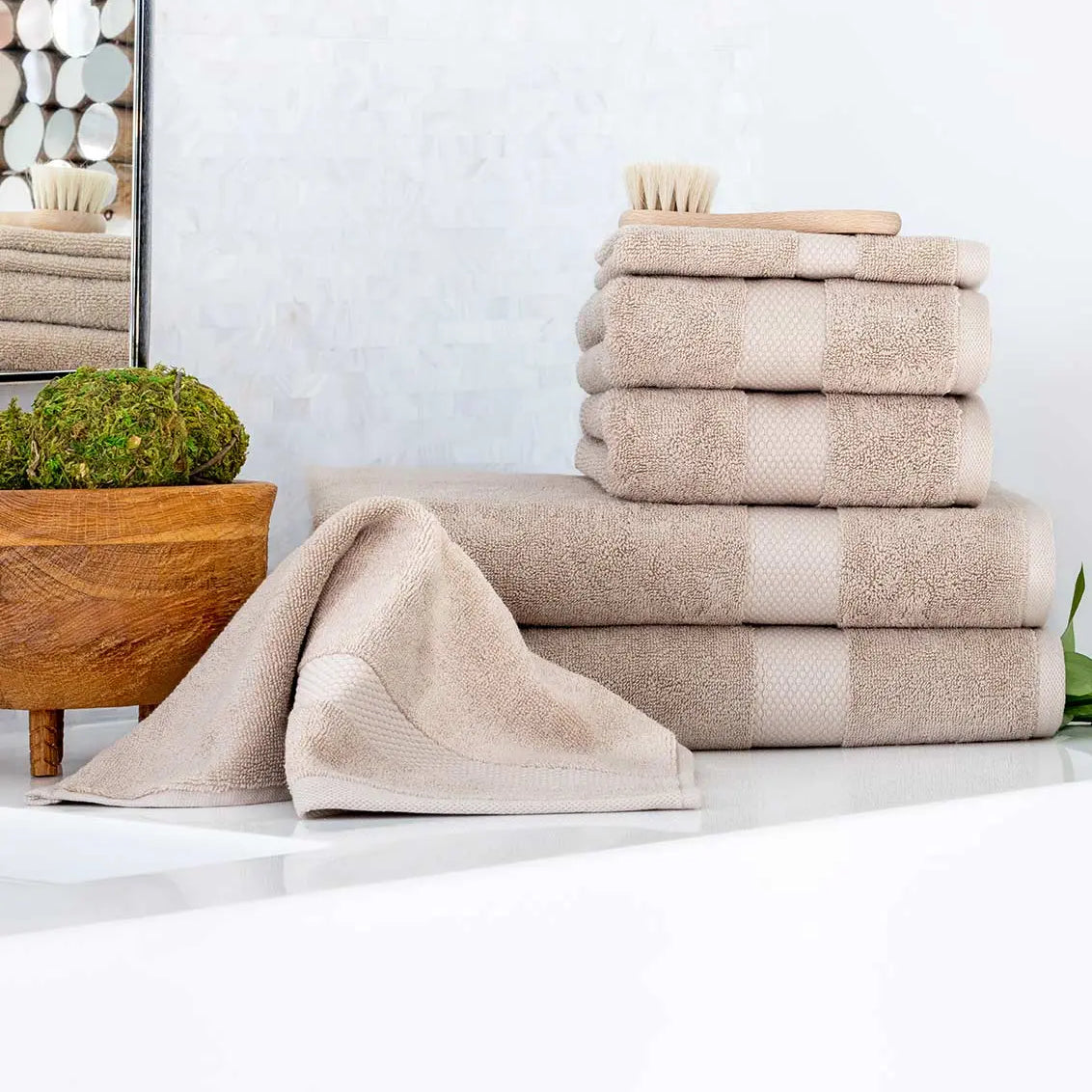 Stack of beige Premium Turkish Cotton towels on a white surface with a mirror and plant in the background