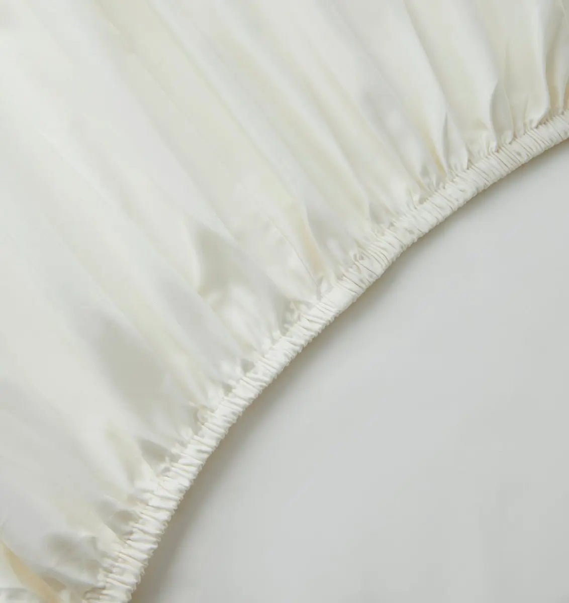 Close-up of an ivory white fitted sheet on a bed with a neutral background