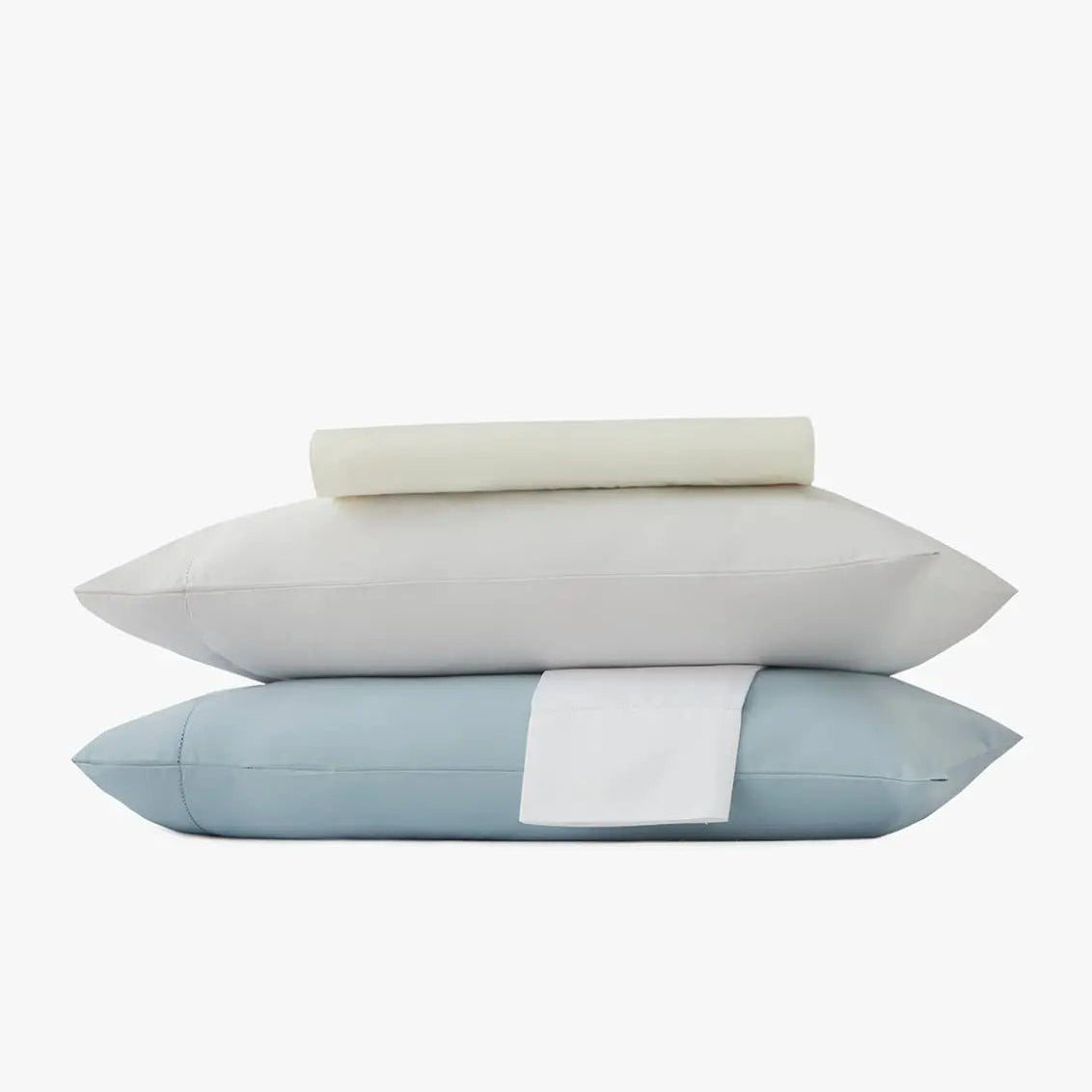 Stack of pillowcases and bed sheets in ivory, white and light blue on a white background