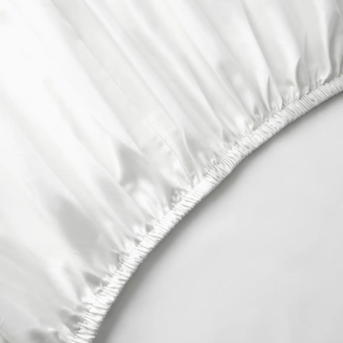 A white fitted bed sheet on a bed with a plain background