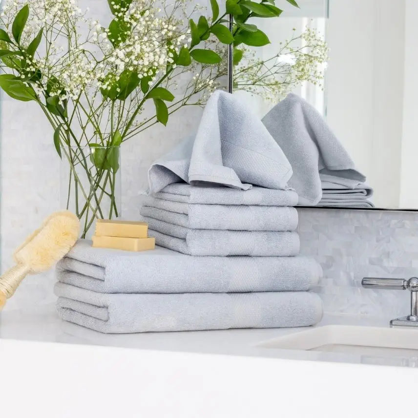 Stack of light blue Premium Turkish Cotton towels on a bathroom counter with a vase of flowers and soap.