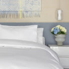 Neatly made bed with white bedding and pillows, nightstand with flowers, and abstract art on wall.