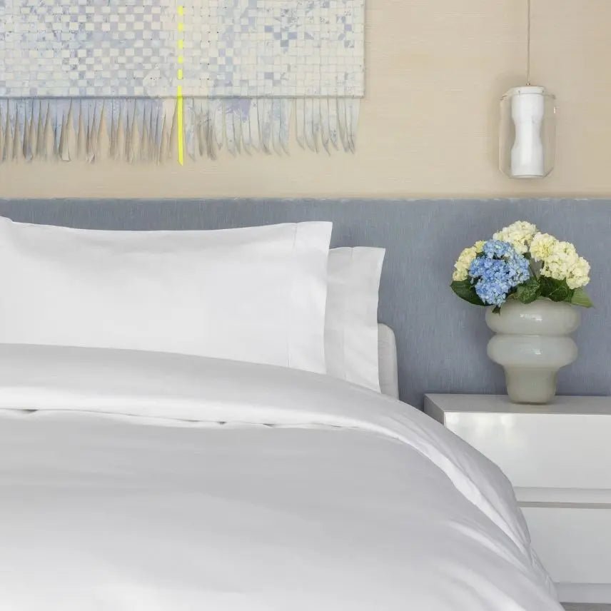 Neatly made bed with white bedding and pillows, nightstand with flowers, and abstract art on wall.