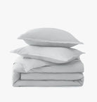 Stack of light gray bedding with two pillows on a white background