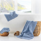 A bathroom with light-blue towels draped over a wooden basket and a wicker basket against a window with a mountain view.