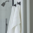 Two white super plush towels hanging from black hangers on a bathroom