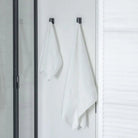 White Turkish cotton towels hanging on black hooks against a white wall.