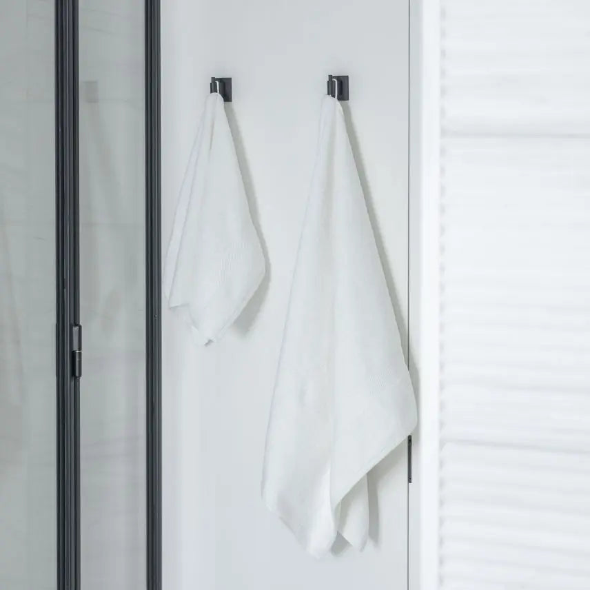 White Turkish cotton towels hanging on black hooks against a white wall.