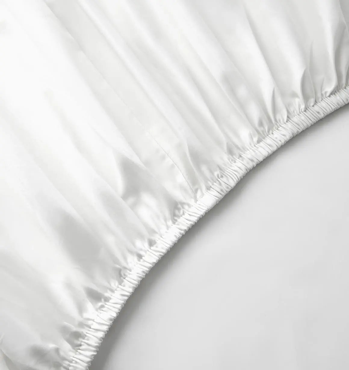 A white fitted bed sheet on a bed with a plain background