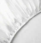 A white fitted bed sheet on a bed with a plain background