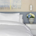 Neatly made bed with a white bed sheet, bedding, and pillows, nightstand with flowers.